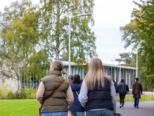 Individuals walking towards a building with trees and nature either side.