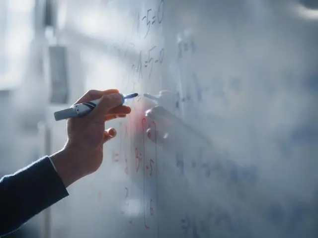 A student writing mathematical equations on a whiteboard